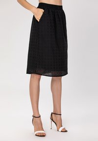 Jupe noire avec une taille élastique, dotée de poches latérales, d'un tissu texturé et d'un ourlet décoratif avec des motifs découpés.