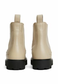 Par de botines de cuero beige con suelas gruesas negras, tiradores traseros y paneles laterales elásticos, vistos desde atrás.