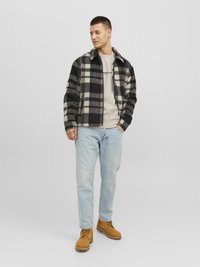 Zwart en beige geruite fleecejack over een beige crewneck, gecombineerd met lichtblauwe jeans en tan suède laarzen. Staande pose.