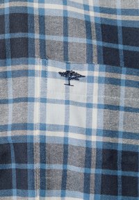 Koszula w kratę o niebiesko-białej kolorystyce z różnymi odcieniami. Na kieszeni na piersi znajduje się haftowane logo drzewa.