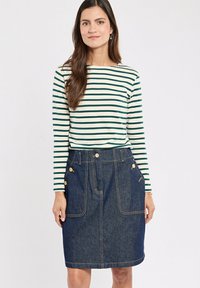 Haut à rayures à manches longues en vert et blanc, associé à une jupe en denim bleu foncé avec deux poches avant et des accents de boutons dorés.