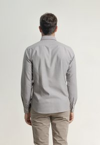 Camisa gris de manga larga hecha de tela suave, con cuello, puños de botones y dobladillo curvado. Combinada con pantalones color beige.