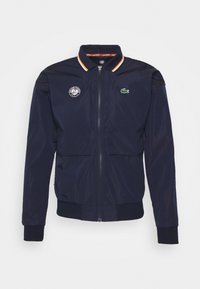 Navyblå zip-up jacka med ribbad mudd och midja, två bröstfickor och en krage med orange och vita ränder.