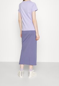 Fialové tričko s kulatým výstřihem v kombinaci s odpovídající dlouhou sukní. Oblečení je vyrobeno z měkké tkaniny, má volný střih a minimální švy.