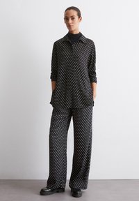 Schwarzes Polka-Dot-Shirt und weite Hose im Set. Weicher Stoff, lange Ärmel, Knopfleiste mit Taschen, kombiniert mit gemusterten Hosen.