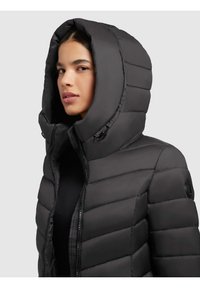 Schwarze Pufferjacke mit großer Kapuze, horizontalem Steppmuster und Reißverschluss. Besitzt ein Logo-Patch am oberen Arm.