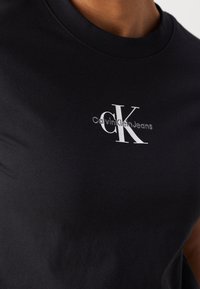 Camiseta de algodón negra con cuello redondo y un diseño del logo blanco de Calvin Klein en el pecho, con una textura de tejido suave.