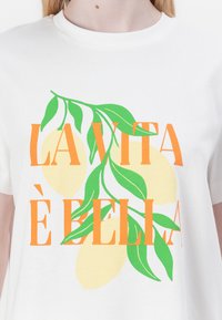 Fehér pamut póló, citromág grafikai elemmel. A színek között szerepelnek zöld levelek, sárga citromok és narancssárga felirat, amely így szól: "LA VITA È BELLA."