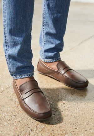 Ruske nahkasaappaat sileällä pinnalla ja minimalistisella muotoilulla. Korostettuna ompeleet ja nauhat yksityiskohtana, yhdistettynä sinisiin farkkuihin.