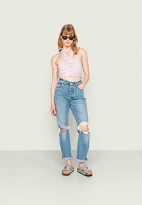 Top curto xadrez rosa e branco com decote halter, calças jeans ligeiramente rasgadas em azul claro com punhos dobrados, sandálias cinzas e óculos de sol pretos.
