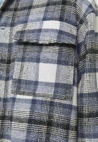 Flannel skjorte med et blått og hvitt ternet mønster, struktureret stof og en brystlomme. Pyntet med varierende gitterdesigns.