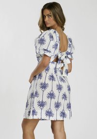 Vestido blanco con patrón de palmeras azules, mangas abombadas y un escote en la espalda con un detalle de lazo en la cintura. Tejido ligero con textura suave.
