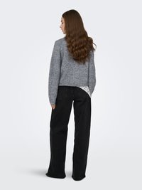 Maglione grigio lavorato a maglia con taglio corto, caratterizzato da un dettaglio in pizzo lungo l'orlo, abbinato a pantaloni neri a gamba larga e vita alta.