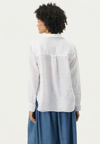 Hvid linned skjorte med lange ærmer, skræddersyet krave, subtil rygf fold og buet kant, parret med en blå denimnederdel.