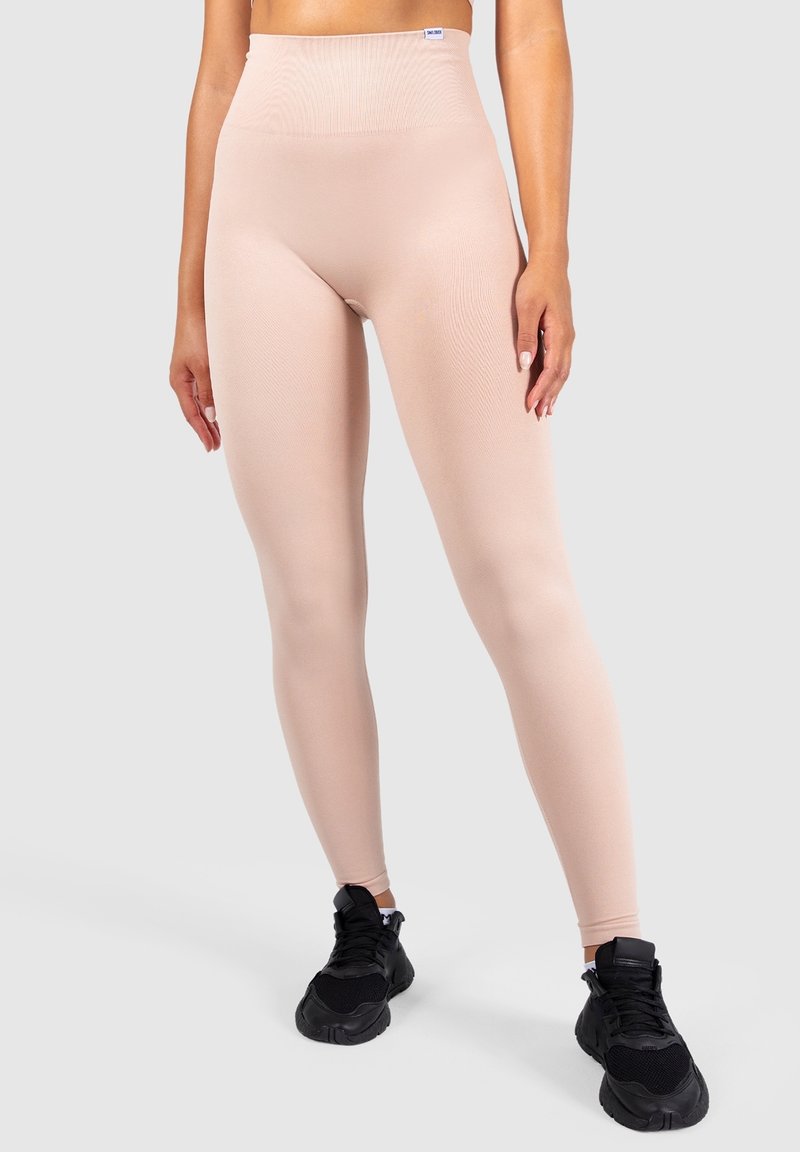 Leggings beige a vita alta realizzati in tessuto elasticizzato, con una cintura a coste e una superficie liscia, abbinati a scarpe da ginnastica nere.
