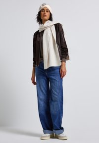 Brun bomberjacka, beige stickad tröja, vida blå jeans, krämfärgad scarf, krämfärgad hårband och beige sneakers med texturerade detaljer.