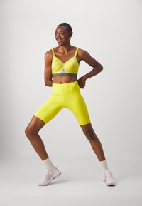Heldere gele sport-bh en bijpassende hoge shorts, gemaakt van rekbaar materiaal, met verstelbare bandjes en een grijze accento.