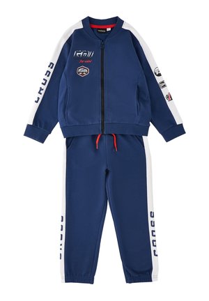 Granatowy dres z białymi paskami na rękawach i spodniach, kurtka na zamek, czerwony sznurek i sportowe logo oraz tekst.