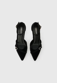 Μαύρες βελούδινες γόβες slingback με μυτερές μύτες, διακριτική λεπτομέρεια λουριού και διακοσμητική ασημένια αγκράφα. Λείος εσωτερικός επένδυσης.