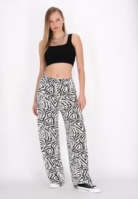 Čierny crop top s širokými, vzorovanými bielymi a čiernymi nohavicami s abstraktnými tvarmi; model má na sebe čierne tenisky; hladký textilný materiál.
