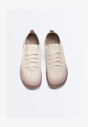 O pereche de adidași bej tricotati cu șireturi, vârfuri rotunjite și benzi maro la călcâi, văzuți de sus pe un fundal alb.