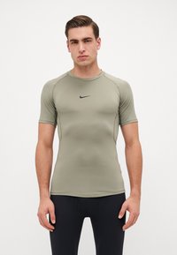 Kortermet treningstopp i olivengrønn, laget av elastisk stoff. Har en ribbet rund hals og svart Nike-logo på brystet.
