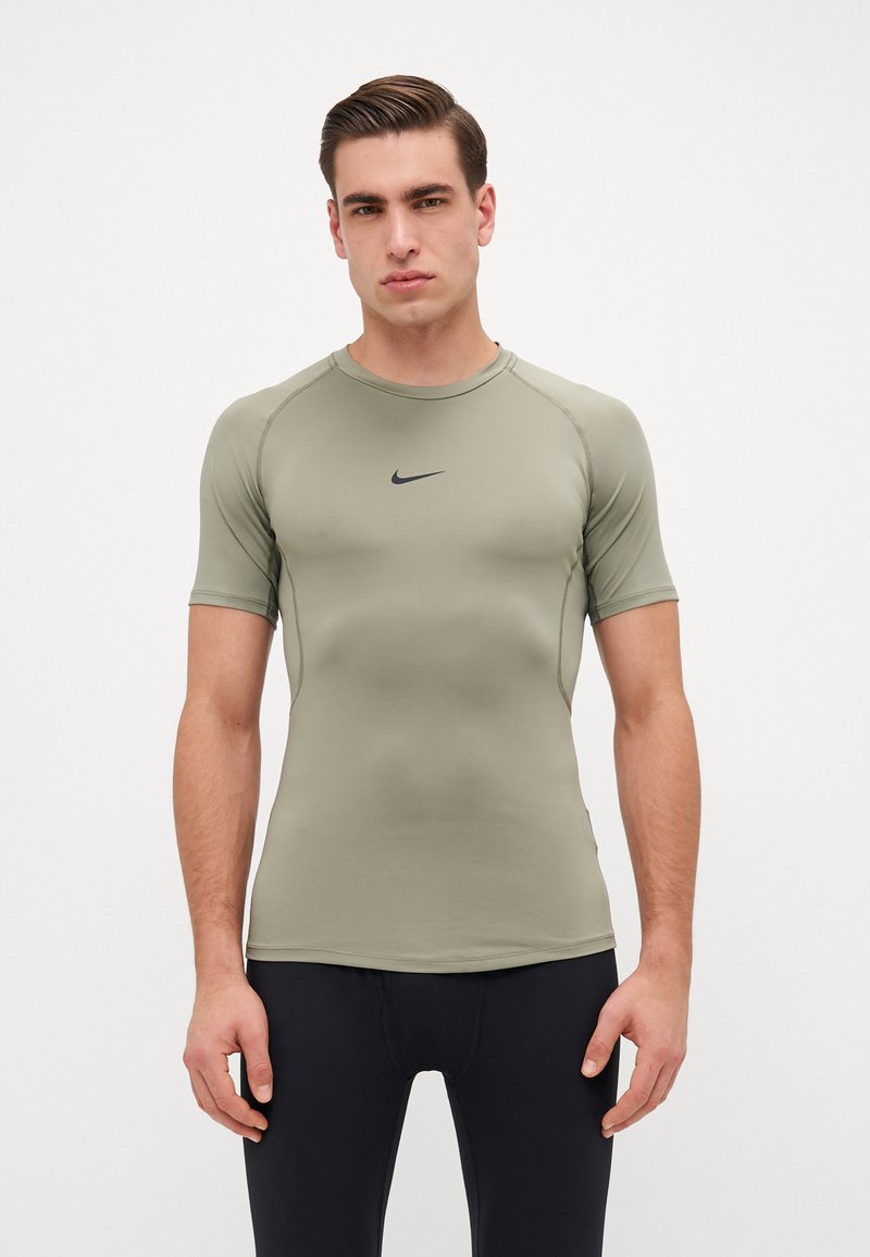 Kortermet treningstopp i olivengrønn, laget av elastisk stoff. Har en ribbet rund hals og svart Nike-logo på brystet.