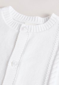 Cardigan en maille blanche avec un col côtelé et un motif texturé le long de la patte de boutonnage. Deux boutons transparents visibles à l'avant.