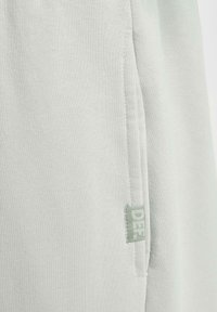 Joggers de algodón verde claro con un bolsillo lateral y una pequeña etiqueta de tela con "DEF" impresa en un tono sutil en el borde inferior.