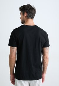T-shirt noir en coton avec un col rond et des manches courtes, présentant une texture lisse et un ourlet droit en bas.