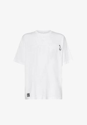 T-shirt bianca a maniche corte con un piccolo cursore nero sul petto in alto a destra e un'etichetta rettangolare nera vicino all'orlo inferiore.
