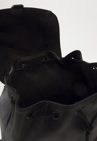 Black drawstring bag made of smooth synthetic material, featuring a soft interior, rounded edges, and simple hardware for closure.