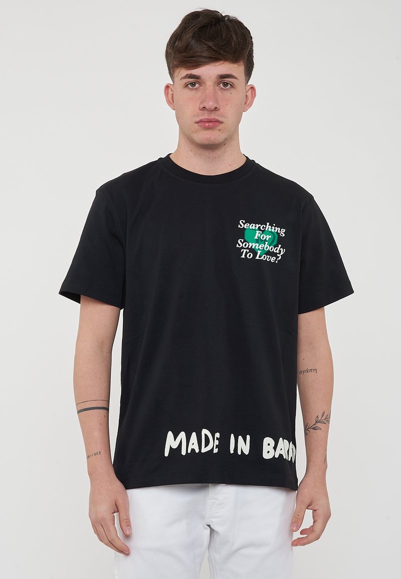 T-shirt in cotone nero con testo verde e bianco che riporta un messaggio grafico sulla parte frontale e "MADE IN BARN" stampato all'orlo.