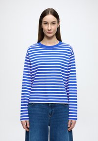 Modrobiele pásikavé tričko s dlhým rukávom, okrúhlym výstrihom a voľným strihom, kombinované so širokými modrými rifľovými nohavicami.