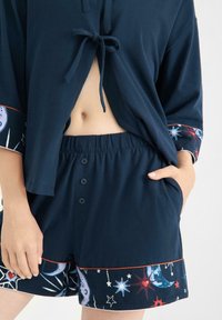 Granatowy zestaw odzieży do wypoczynku wykonany z bawełny, z topem wiązanym z przodu oraz szortami zapinanymi na guziki, ozdobiony kolorowymi wzorami kosmicznymi i elastycznym paskiem.