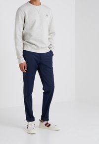 Felpa in cotone grigio chiaro con scollo rotondo, pantaloni sartoriali blu scuro e sneakers bianche con dettagli in bordeaux. Design semplice e moderno.