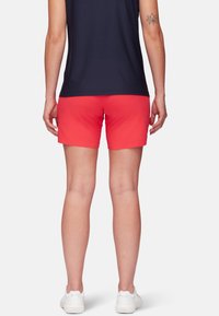 Pantalones cortos deportivos rojos con una textura suave, de tiro medio y color sólido, combinados con zapatillas blancas y una camiseta azul marino.