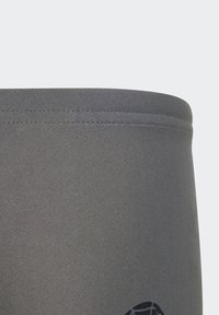 Fascia elastica grigia con una sottile trama a coste e dettaglio decorativo grafico nero. Il materiale sembra liscio ed elastico.