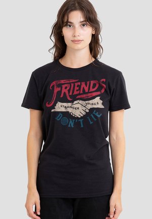 Junge Frau trägt ein schwarzes T-Shirt mit einem Handschlag-Motiv und dem Text "Freunde lügen nicht", eine Anspielung auf Stranger Things.