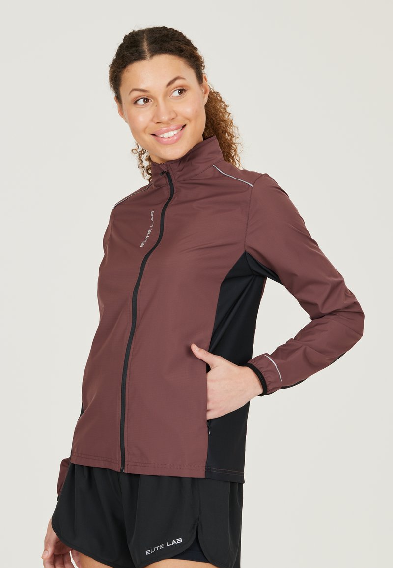 Veste de sport bordeaux et noire avec un col montant, fermeture éclair et détails réfléchissants, fabriquée en tissu léger et respirant.