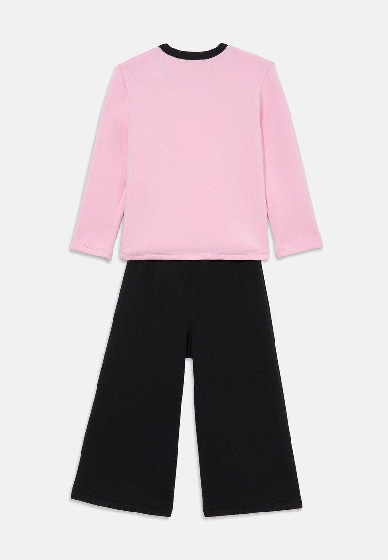 Maglietta a maniche lunghe rosa con colletto nero abbinata a pantaloni neri a gamba larga. Tessuto morbido, vestibilità comoda e senza motivi o accessori visibili.