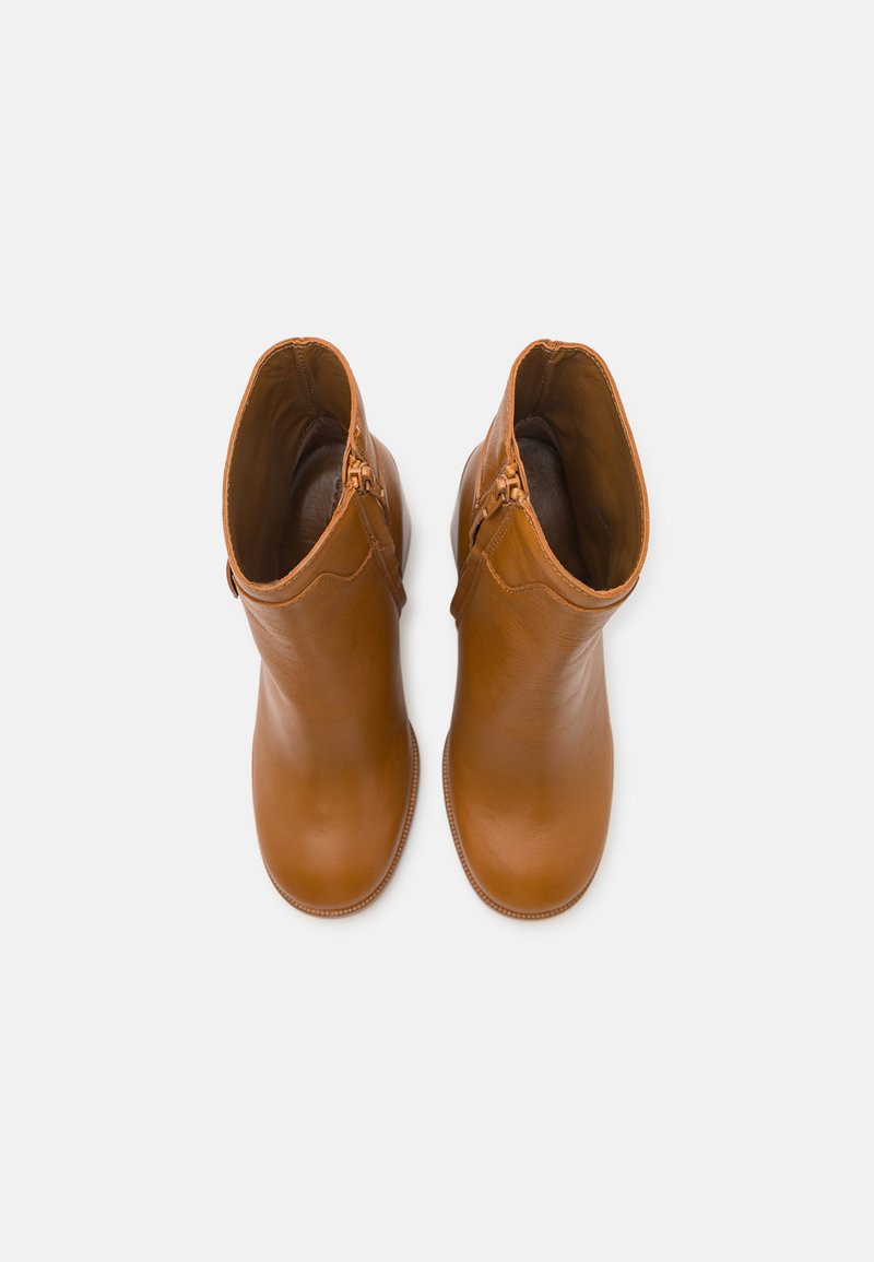 Une paire de bottines en cuir lisse beige avec des fermetures éclair sur le côté, vues de dessus sur un fond blanc uni.