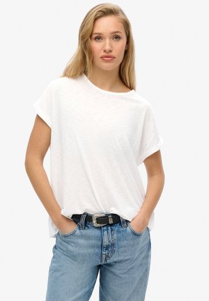 Witte T-shirt met korte mouwen en een losse pasvorm, gecombineerd met lichtblauwe spijkerbroek en een zwarte riem met een zilveren gespdetail.
