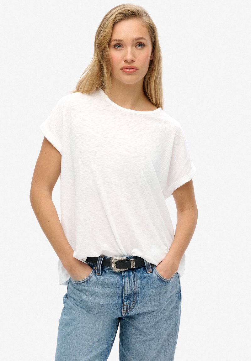 Witte T-shirt met korte mouwen en een losse pasvorm, gecombineerd met lichtblauwe spijkerbroek en een zwarte riem met een zilveren gespdetail.