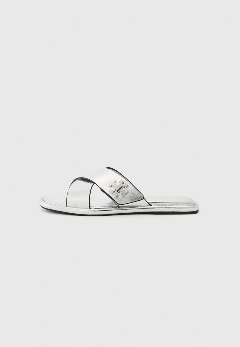 Ezüst szandálok nyitott orral, fényes felülettel, keresztpántos kialakítással és dombornyomott logóval az oldalon.