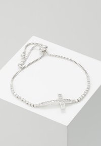 Sidabrinė apyrankė su kryžiaus dizainu, papuošta skaidriais brangakmeniais, papildyta lanksčia grandine ir reguliuojamu užsegimu.