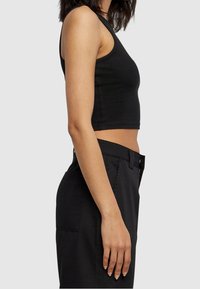 Svart ribbad crop top med breda band, figurnära design och slät textur, i kombination med högmidjade svarta byxor med sidofickor.