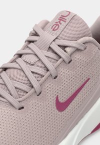 Világos rózsaszín sportcipő, lélegző hálós felső résszel, texturált dizájnnal, lapos fűzőkkel és ellentétes sötét rózsaszín Nike logóval az oldalon.