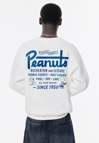 Witte sweatshirt met een blauw grafisch tekstontwerp waarin "Peanuts" en cartoonfiguren zijn afgebeeld. Geribbelde manchetten en zoom.