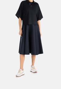 Polo corto blu navy con maniche corte abbinato a una gonna svasata coordinata e scarpe da ginnastica leggere con accenti rosa e grigi.